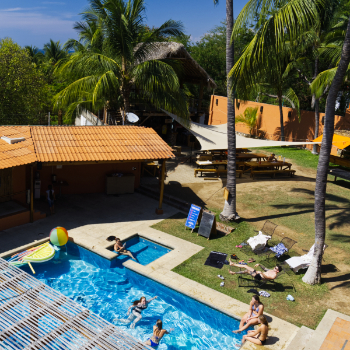 A shot from above, people hang out in the pool and lounge under the palm trees at Bonita Hostel in Puerto Escondido.