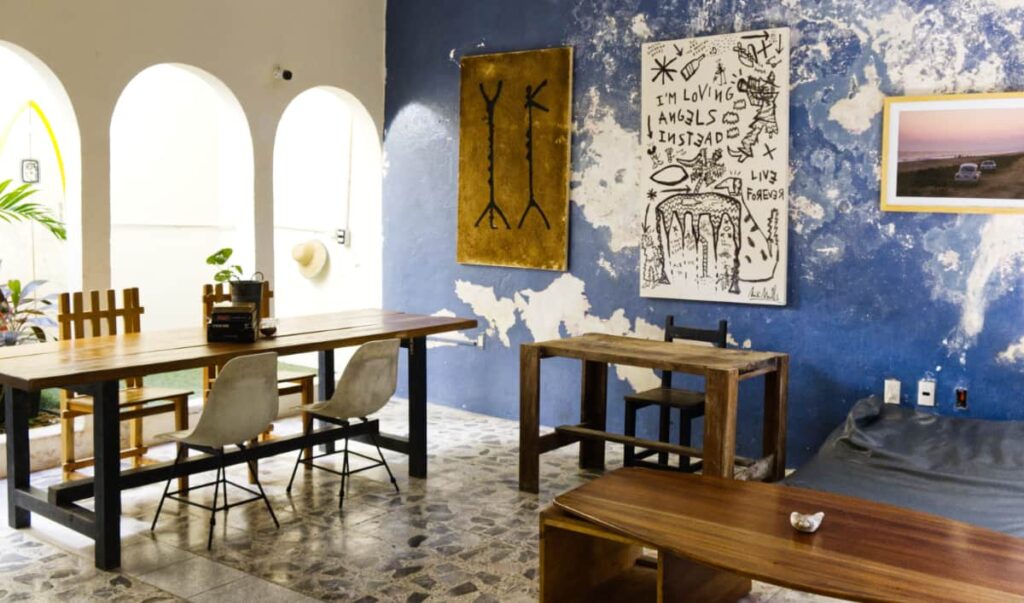 Several tables and chairs make a nice workspace at Puerto Dreams Hostel while several pieces of art decorate the blue wall.