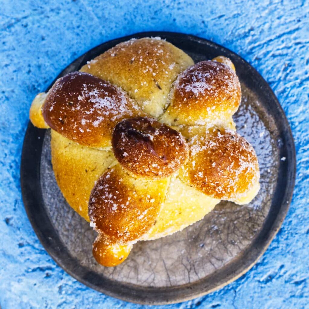 An overhead shot of pan de muertos which is dome shaped and characterized by bone-like formation with a dusting of sugar on top.