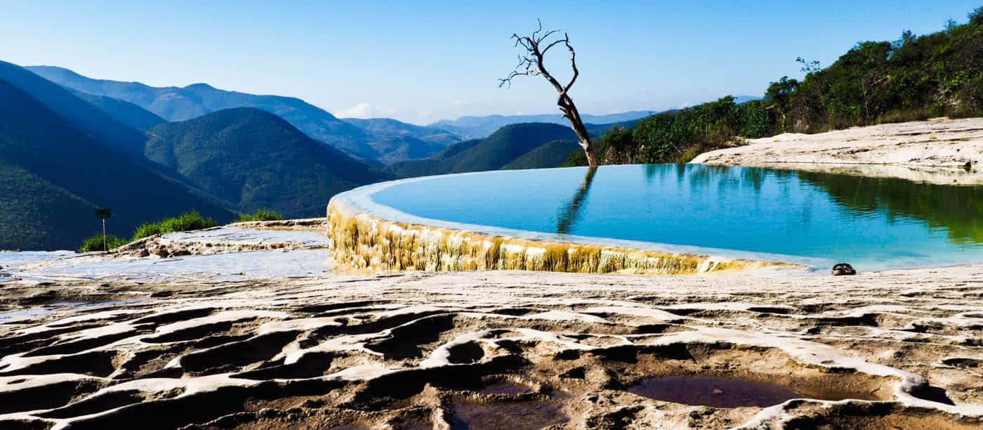 A panoramic view of the blue infinity pool at Hierve el Agua with surrounding mountains.