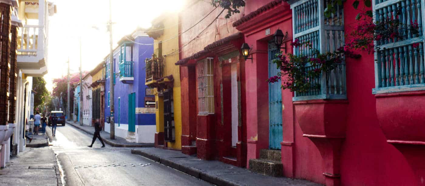 Colorful buildings with brightly colored accents, wood details, and tropical plants line the street in Cartagena, Colombia.