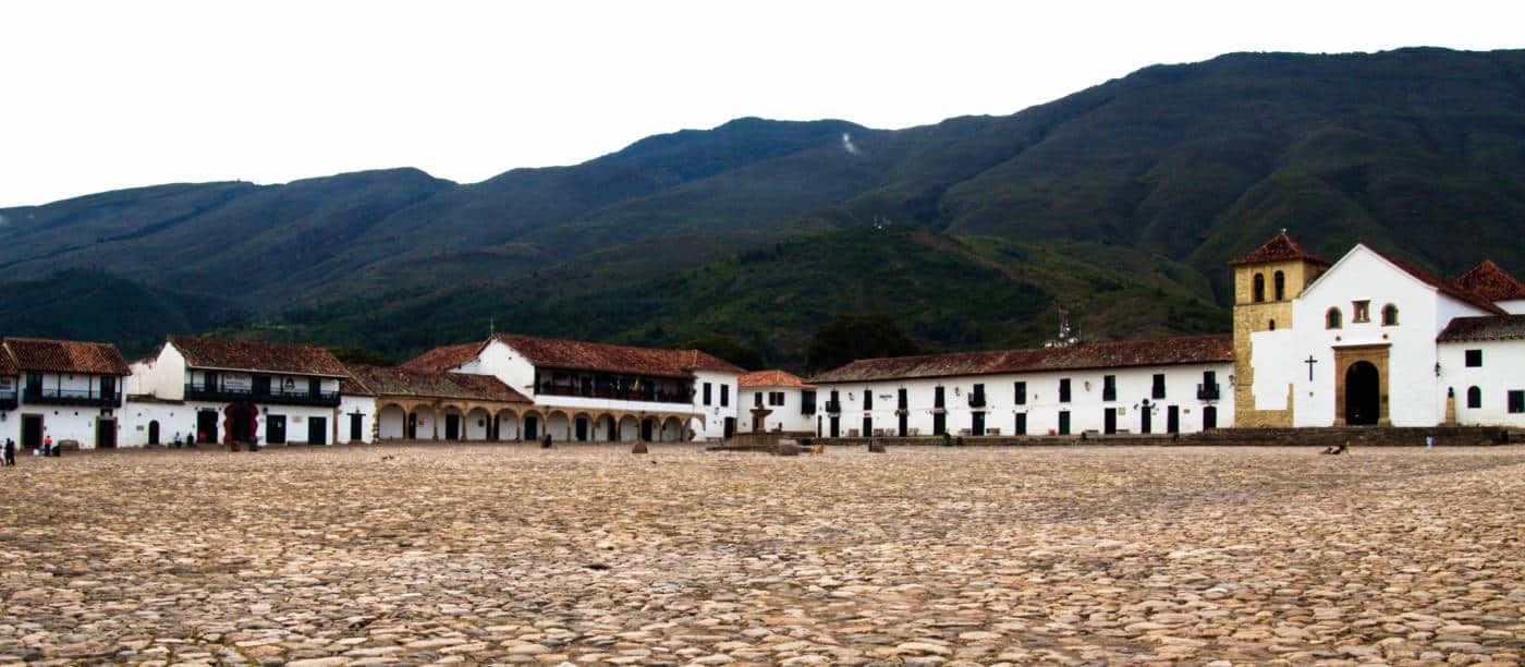 Wide Angle view of the cobbled square in Villa de Leyva. White colonial buildings, including the main church, and green mountains surround.