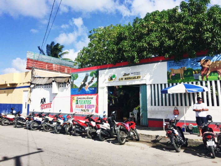 Street view of Managles, a great cantina in Cozumel. Scooters and motorcycles are lined up with an attendant to watch over. Buckets of Tecate are advertised for 150 pesos.