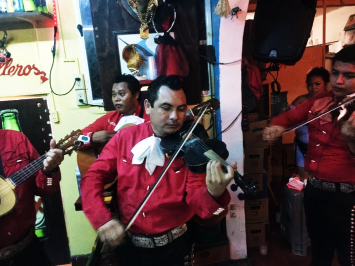 A mariachi band dressed in red button down shirts and black pants play string instruments at one of the best cantinas in Cozumel, La Revancha.