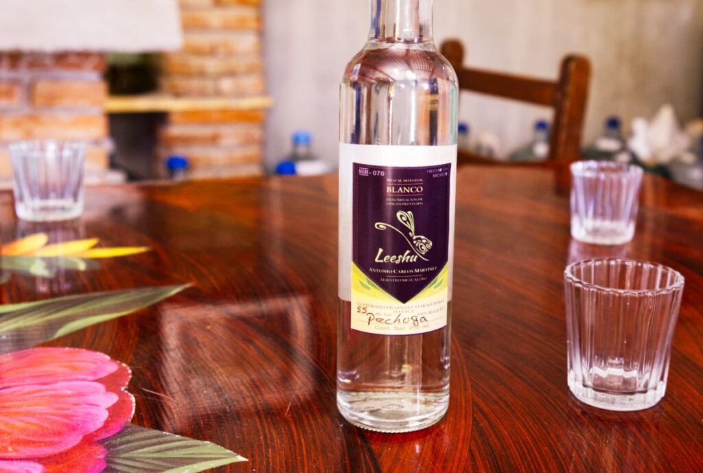 A bottle of pechuga mezcal sits on the table with several tasting glasses nearby.
