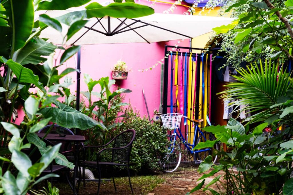 In the garden at Azul Cielo Hostel, Oaxaca a bike leans against the gate. The garden is full of tropical plants and a table with umbrella.