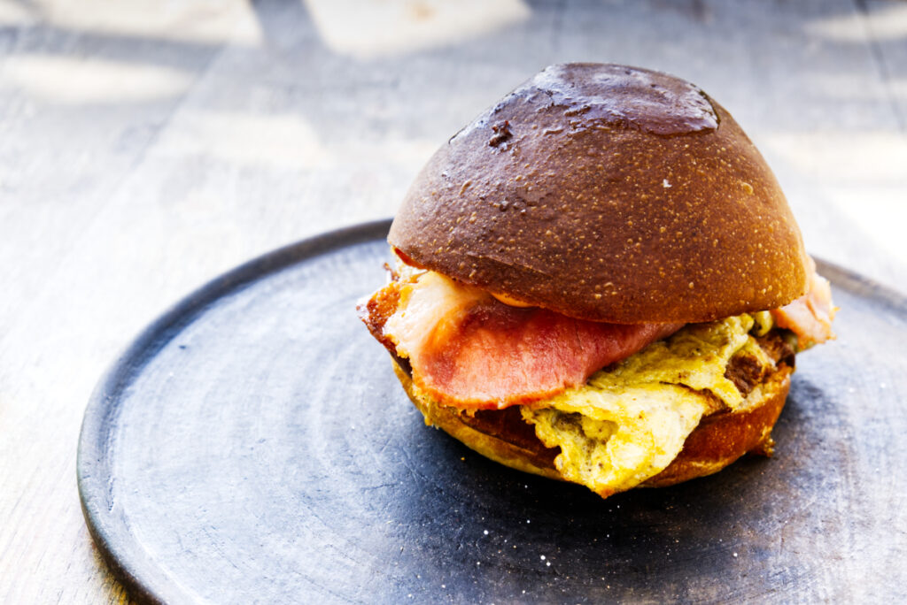 A scrambled egg and bacon sandwich on a round black clay plate is one of the best brunch in Oaxaca.