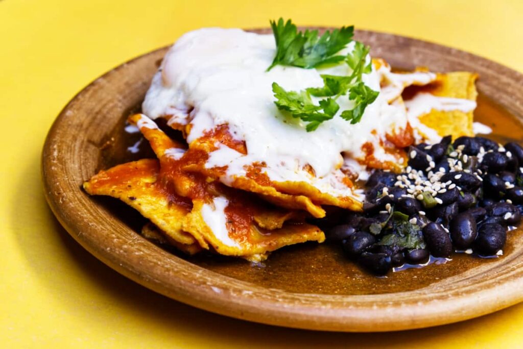 A rustic plate is filled with chilequiles and served with a side of whole black beans.