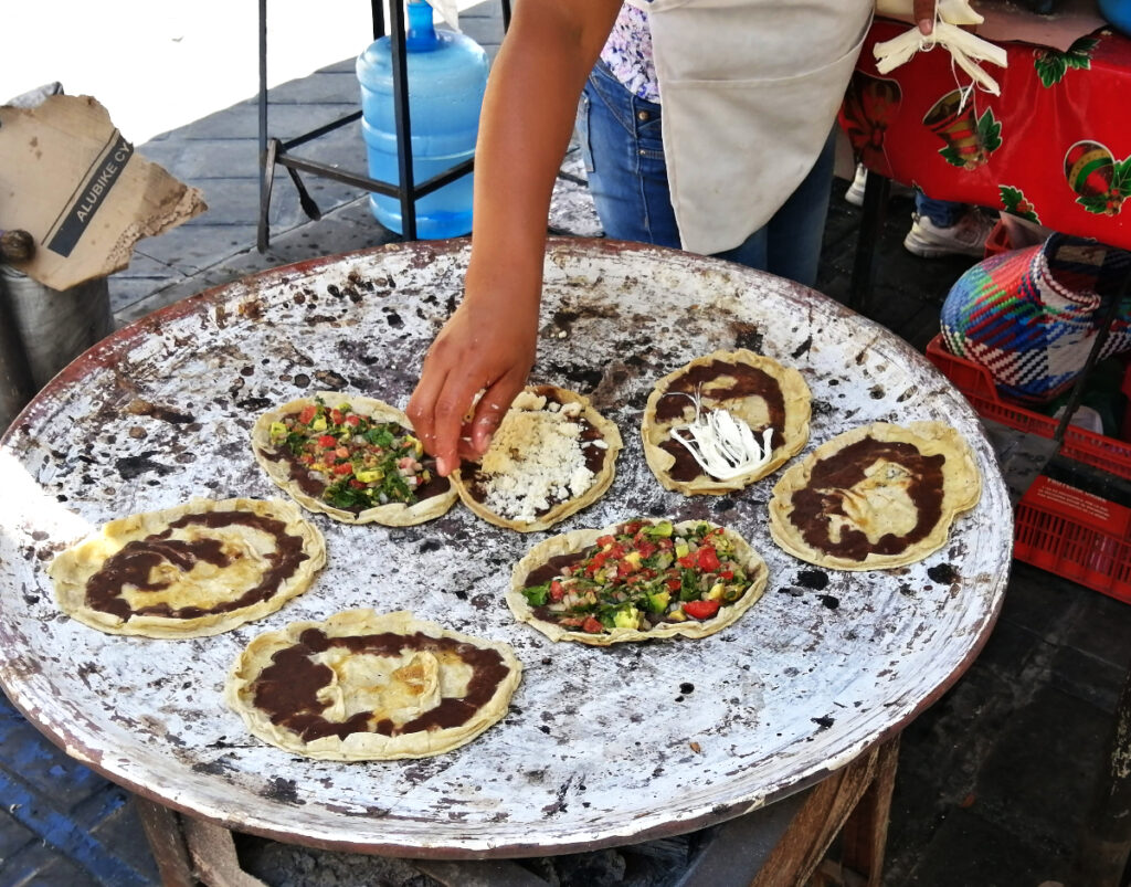 A woman reaches to tend to the large round comal where she is cooking memelas, the ultimate cheap breakfast in Oaxaca.