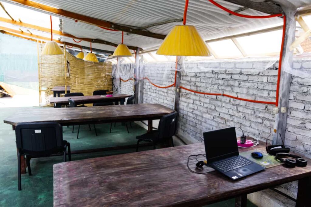 At the co-working space, three long wooden tables sit on the covered rooftop. On one is a black laptop, mouse, and headphones.