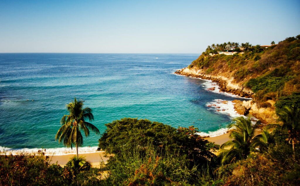 Golden sand, turquoise waters, tall palms, and a rocky cliff face encompass this overview shot of Playa Carrazalillo, a great relief from the hot and humid weather in Puerto Escondido.