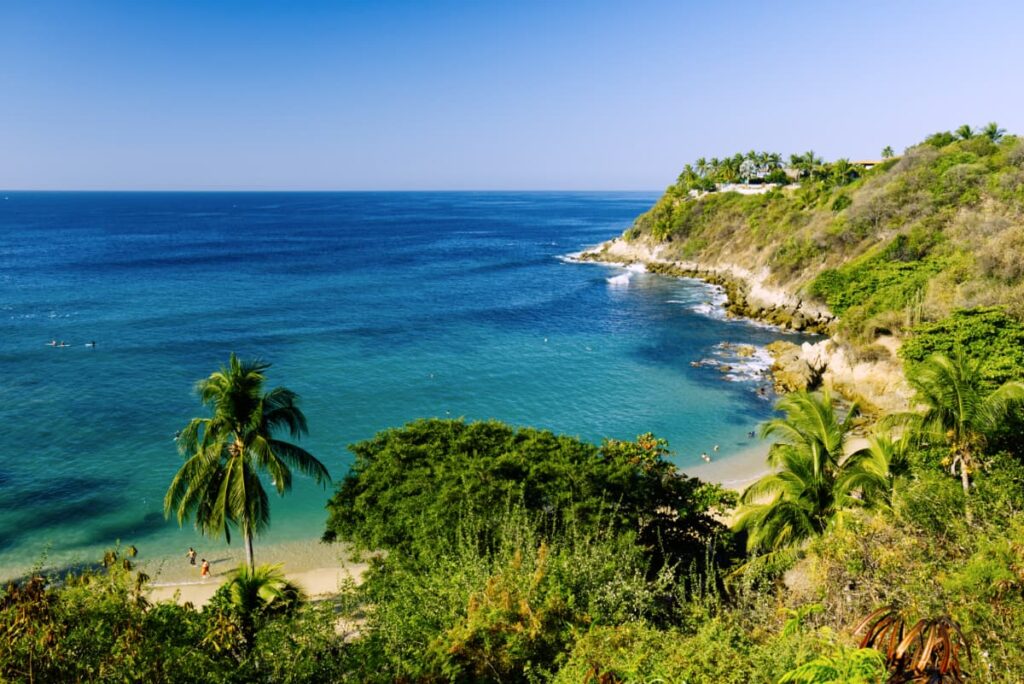 At one of the most beautiful Puerto Escondido beaches, turquoise waters, rocky cliffs, and tall palms create an inviting area to swim.