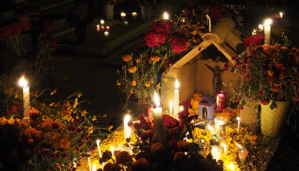 At a Cemetery in Oaxaca for Day of the Dead, a gravesite is topped with a variety of lit candles and vases of traditional flowers.