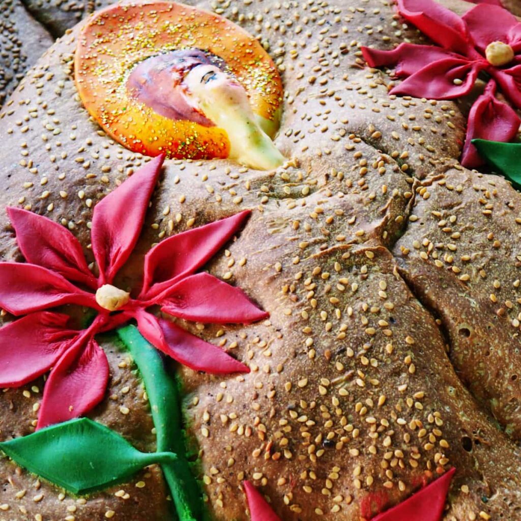 A close up view of the Oaxaca Day of the Dead Bread which is decorated with red flowers and the face of a woman.