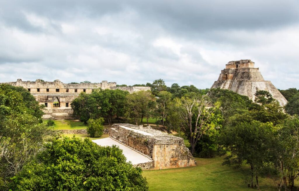 An overall view of Uxmal, one of the most underrated Yucatan ruins. In the foreground is the ballcourt and in the background, the Pyramid of the Magician which is tall with unusually rounded corners.