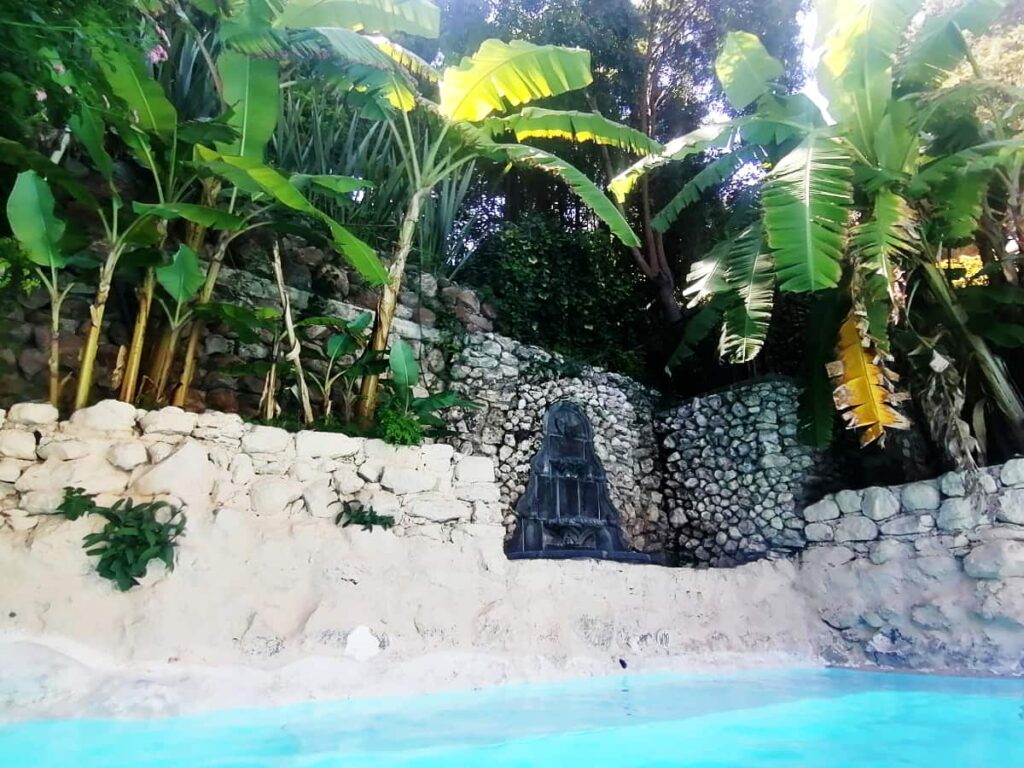 Banana trees and other lush vegetation surround on of the hot spring pools at La Gruta Spa, the most relaxing day trip from San Miguel de Allende. The pool is constructed of off-white rocks.