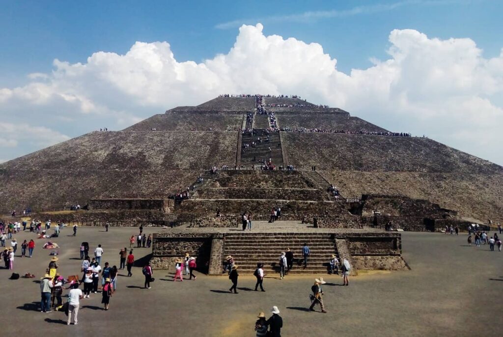 A frontal view of the Pyramid of the Sun while people visiting Teotihuacan from Mexico City stroll the grounds and climb on top of the pyramid.