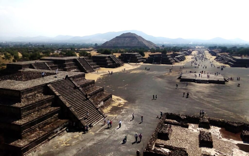 A view of the Pyramid of the Moon and other Teotihuacan pyramids from atop the Pyramid of the Sun. In the background, people are seen strolling along the long pathway known as the Avenue of the Dead.