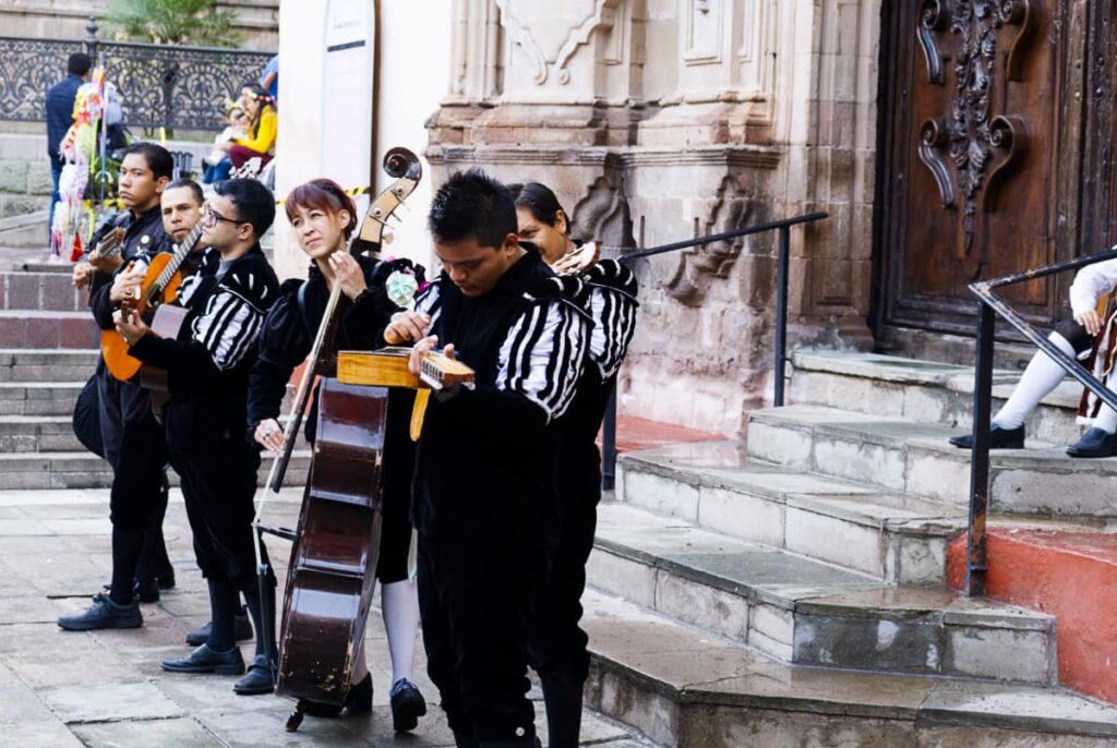To start the callejoneada, young musicians play string instruments in front of a church in Guanajuato. They are dressed in medieval costume of black and white color.