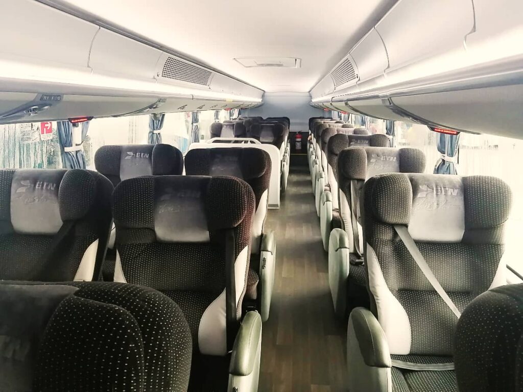 Inside an ETN bus, one of the main bus lines in Mexico, there are plus grey seats with overhead bins above. The seats are arranged two on one side and one on the other.