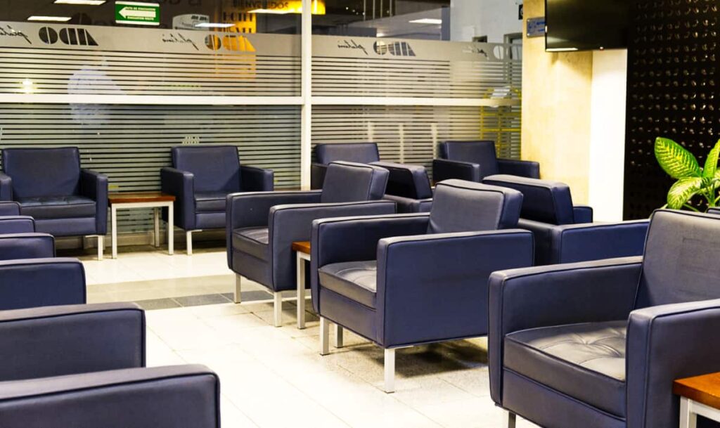In the ADO luxury bus waiting room, blue chairs and wooden tables sit empty. These waiting rooms are available for passengers of the first class buses in Mexico.