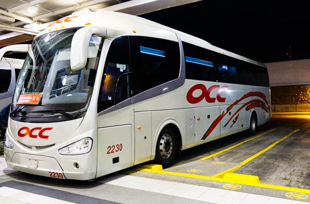 Waiting to depart from a bus station in Mexico, the OCC bus is parked and lit up.