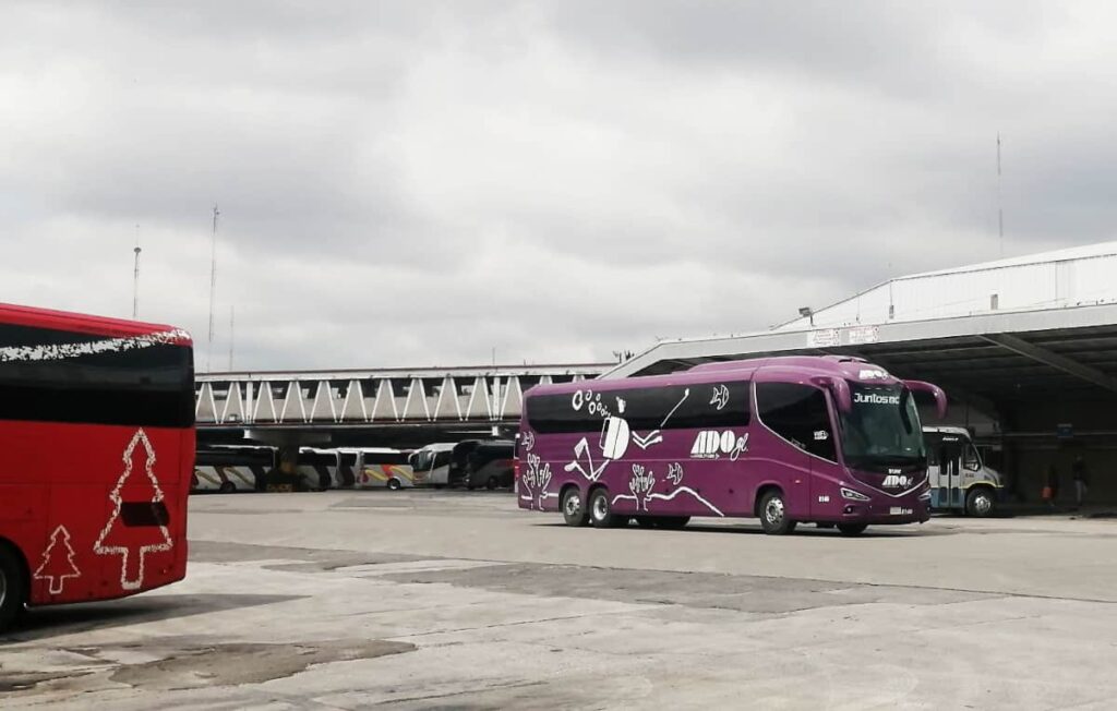 In the parking lot of a bus station in Mexico, a luxury bus called ADO gl passes by while another ADO bus is parking on the side.
