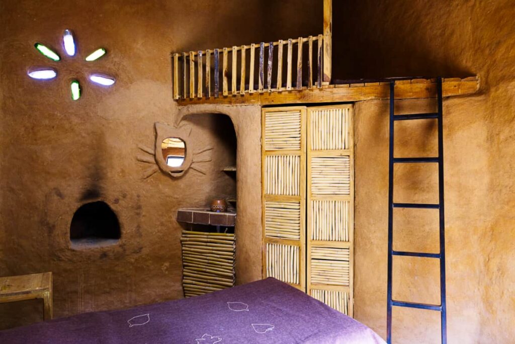 The cabanas at Cuatro Palos feature orange clay walls with natural finishes like wood and clay reeds to make the door. A ladder leads up to a small loft and recycled bottles are used in the wall to let light in.