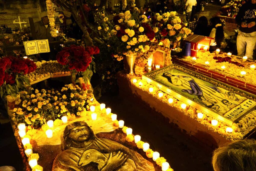 At one of the Oaxaca cemetery for Day of the Dead, gravesites are decorated with intricate biblical scenes created from colored sand and glitter, called tapetes. Surrounding the graves are votive candles and flowers.