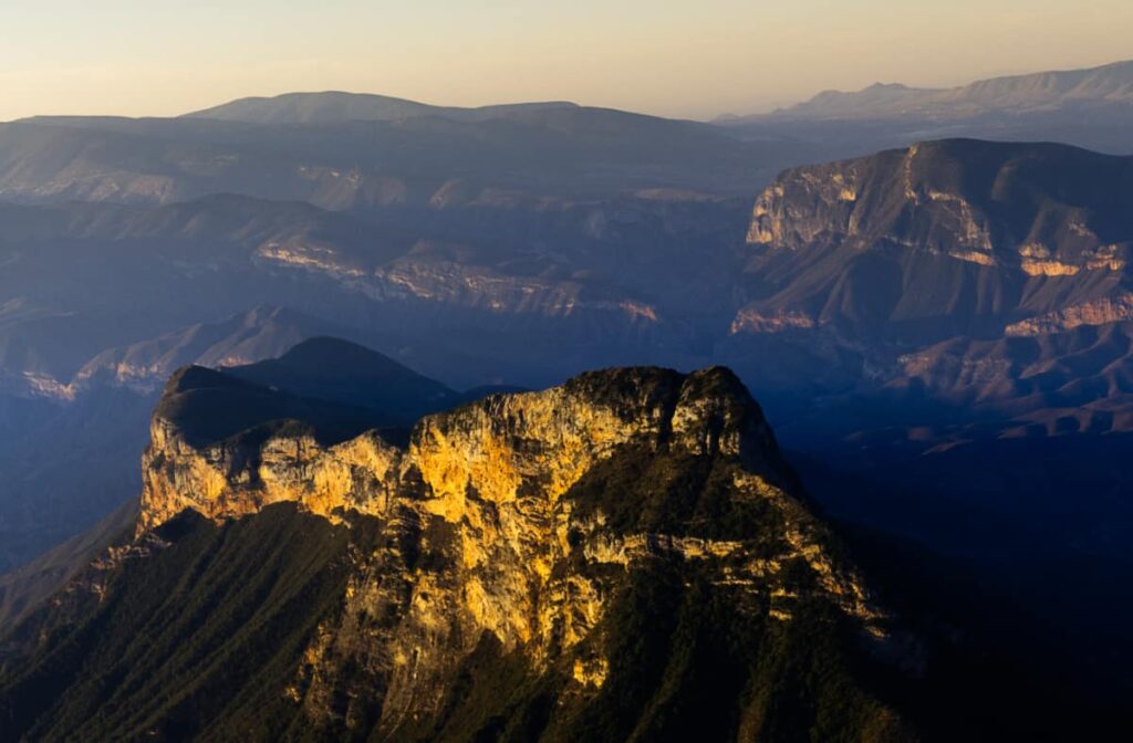 Mirador Cuatro Palos as the rising sun baths the rugged rock in warm light. In the background are other rugged green mountains.