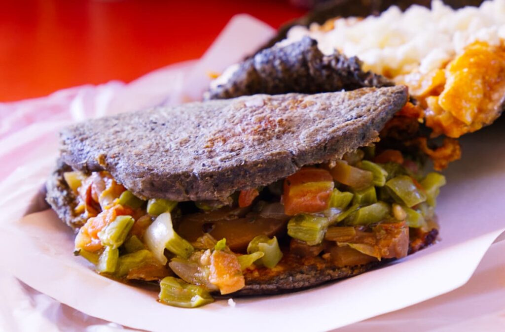 A closeup picture of a blue corn gordita stuffed with vegetables.