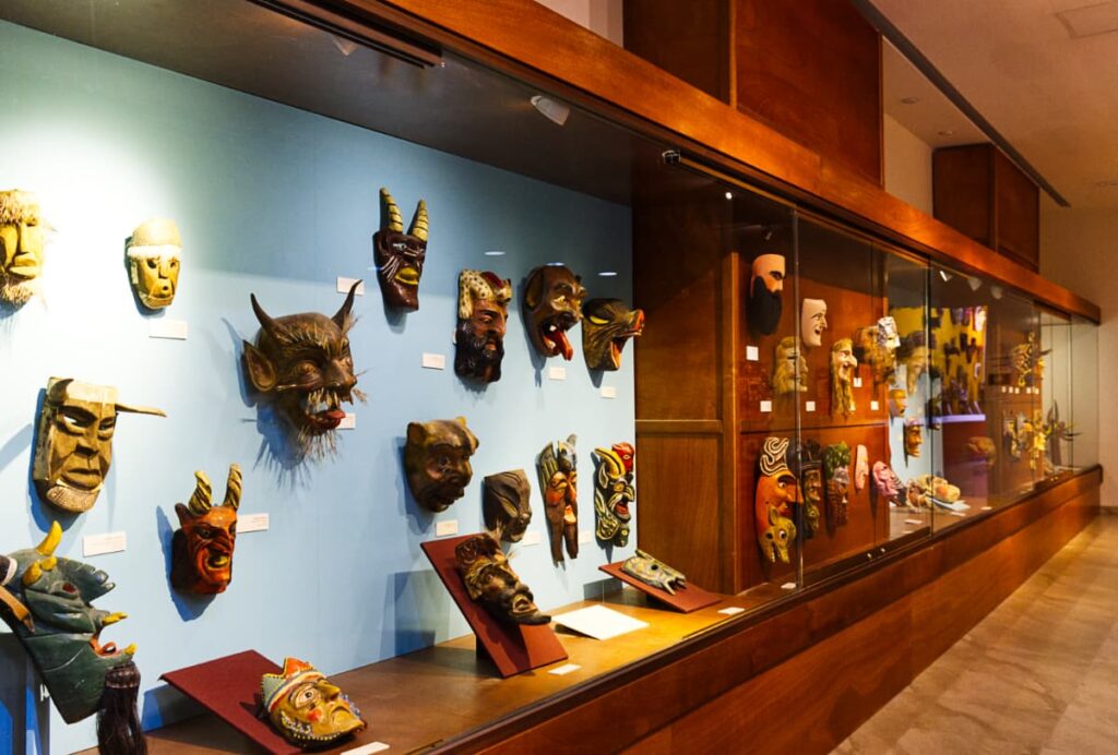 Inside the mask museum in Bernal Queretaro. Various masks hang on the wall behind a glass display.