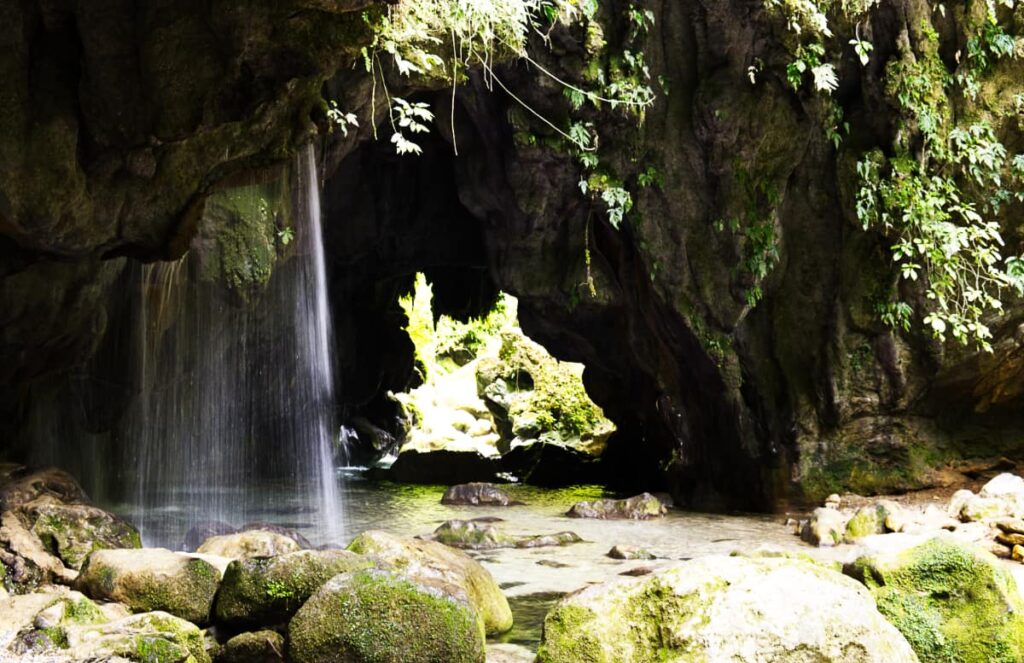 A stream of water flows through the rock cave of Puente de Dios Queretaro. In the background you can see light coming through the back opening of the cave.