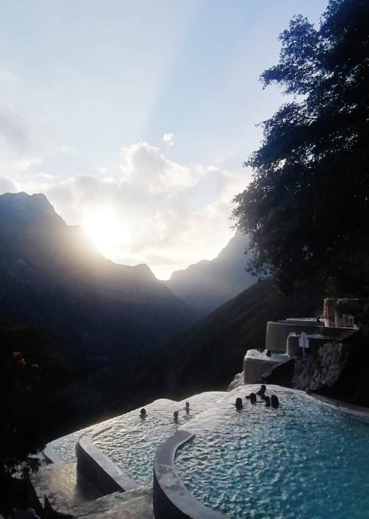 Several people swim in one of the manmade hot spring pools at Grutas Tolantongo, Hidalgo as the rising sun peaks above the mountains.