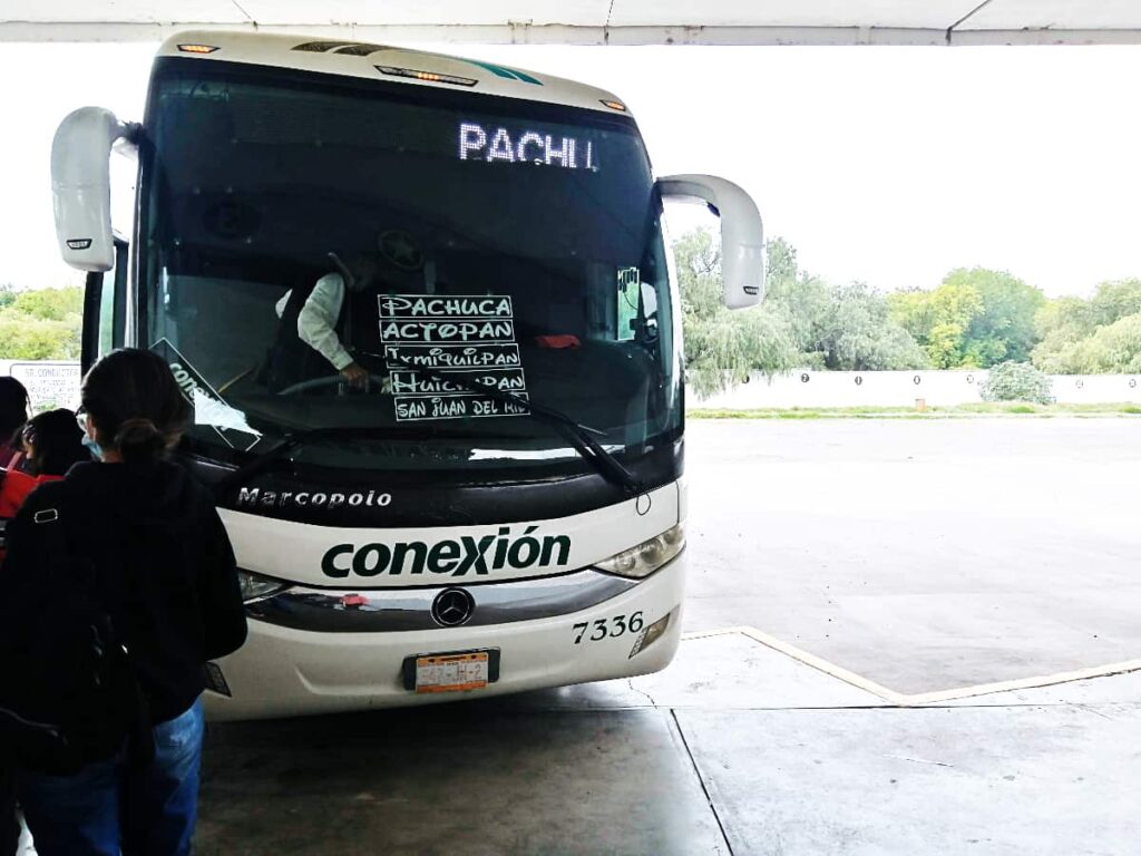 Several people stand in line to board the bus to Ixmiquilpan, Hidalgo. A sign in the front windshield lists the destinations along the route.