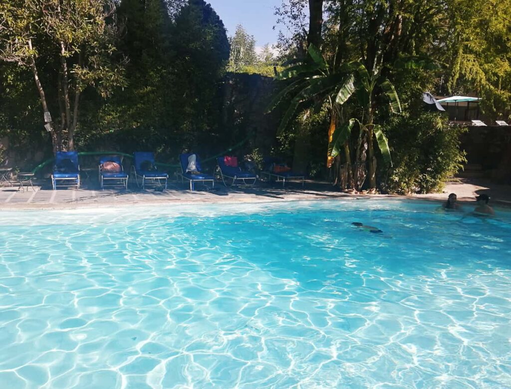 One of the pools at La Gruta hot springs features bright blue water with several people swimming. Surrounding the hot spring pool are lounge chairs and plants.