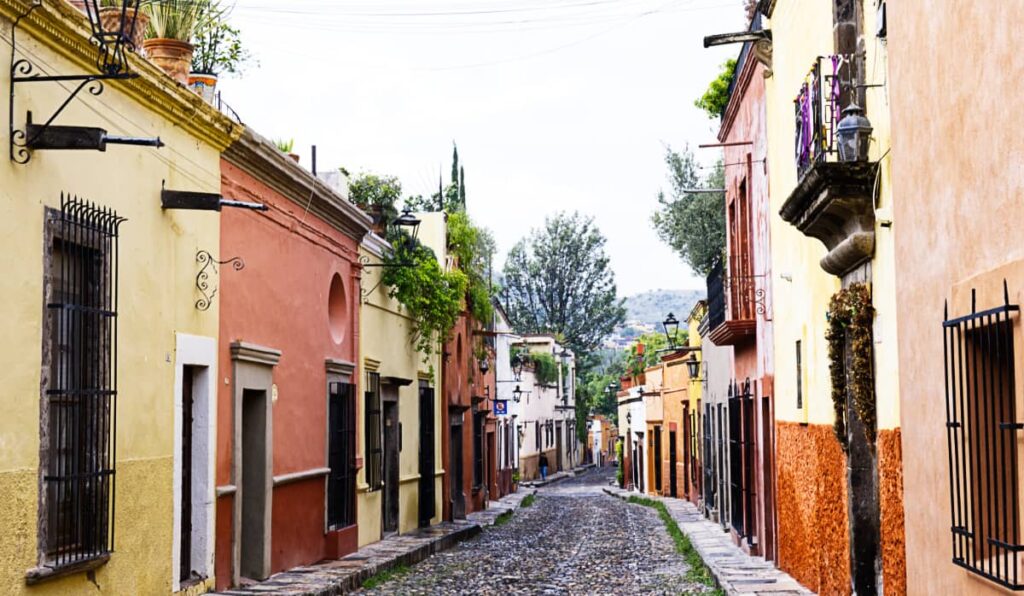 A cobblestone street in San Miguel de Allende with houses painted in oranges, yellows, and white along the side.