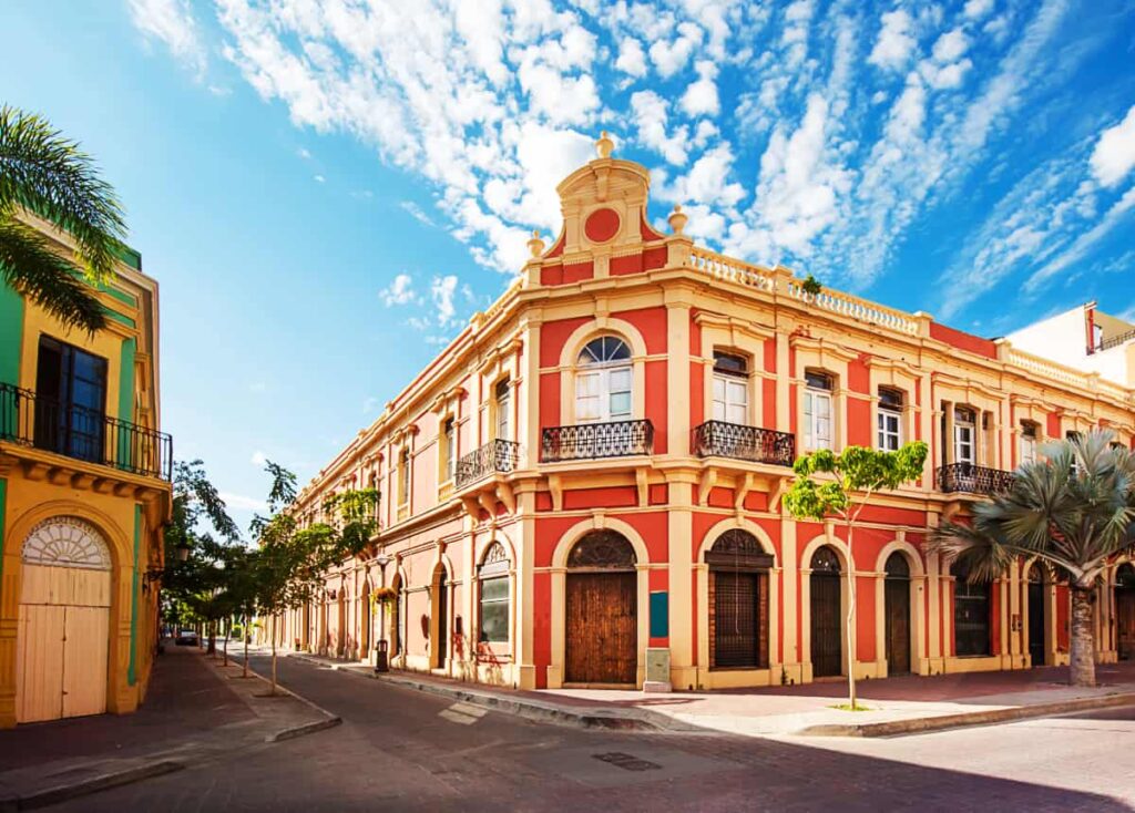 A coral colored building with multiple arches is located on an urban corner of Mazatlan, Mexico.