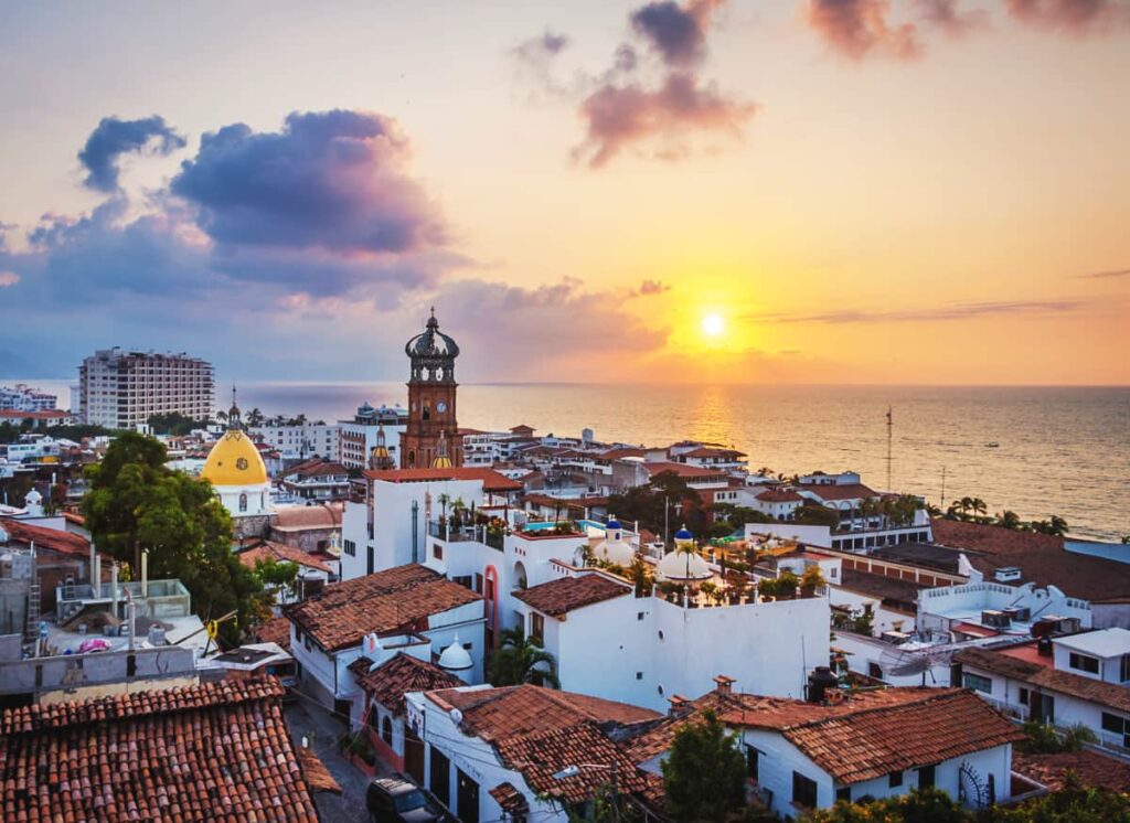 The sunsets over the ocean in Puerta Vallarta, one of the most beautiful cities in Mexico. In the foreground are beautiful white buildings with red tile roofs.