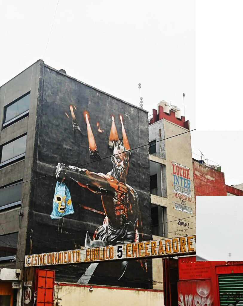 Outside of Arena Mexico, the main arena for lucha libre in Mexico City, the side of a building is shown with street art of a Mexican wrestler holding his mask in his hand out to the side.