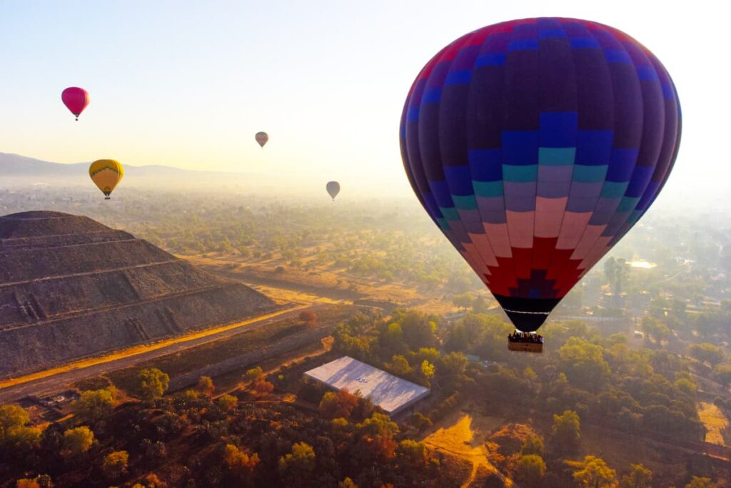 An up close view of a Teotihuacan hot air balloon as it rides over the pyramids. In the background are several more colorful hot air balloons over Teotihuacan.