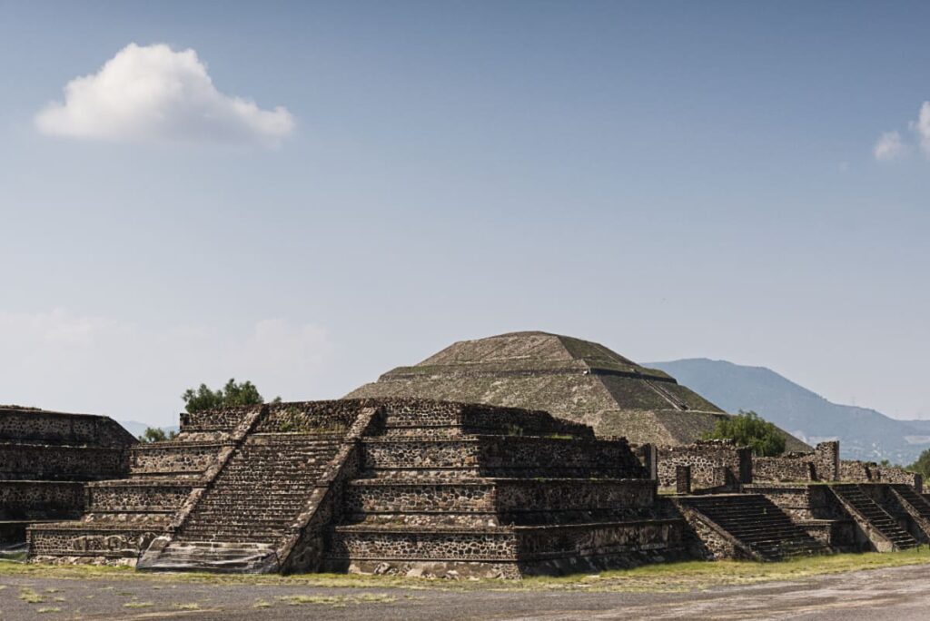 A profile view of the pyramids during a Teotihuacan tour from Mexico City. In the background are a stepped mountain side which is believed to have inspired the shape of the Pyramid of the Sun to be strong in an earthquake.