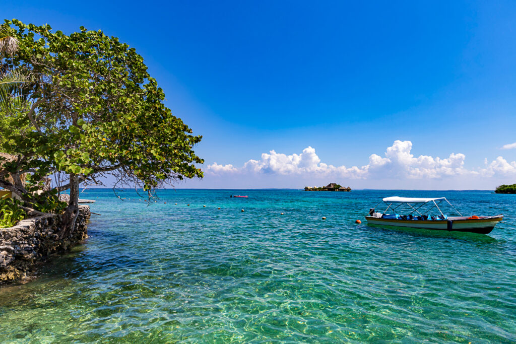 During the best boat tours in Cartagena, a boat is anchored in the shallow blue waters of Islas del Rosario, Cartagena Colombia.