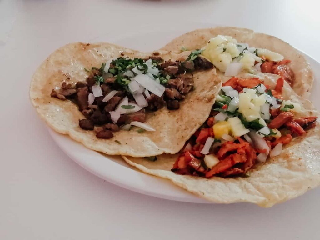 A plate from the best taco tour in Mexico City includes three different types of tacos including al pastor and bistec. They are topped with onion and cilantro.