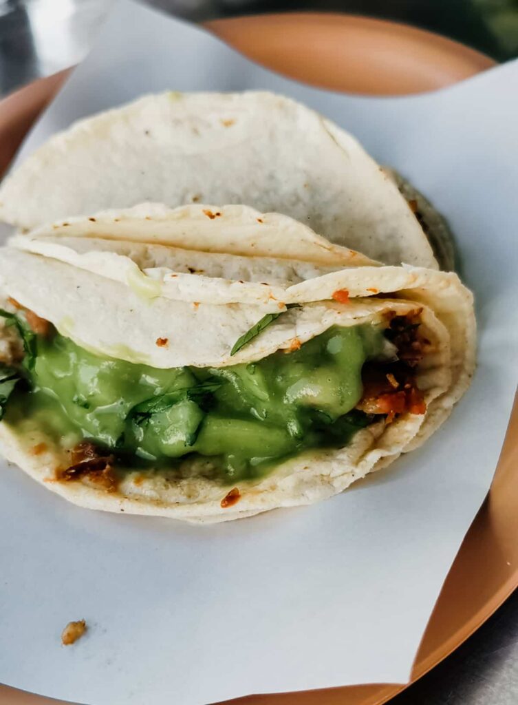 During a taco tour in Mexico City, a plate of two small tacos de cabeza topped with avocado salsa.