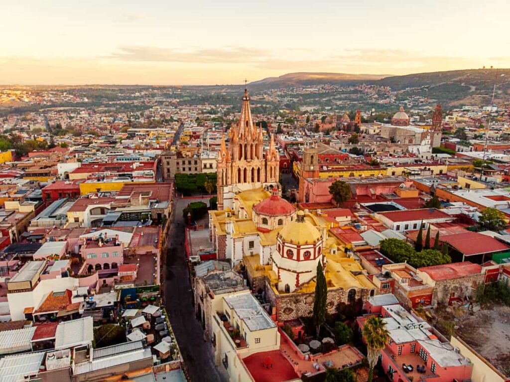 An overview shot of San Miguel de Allende from a hot air balloon shows the back of the main church, the streets of the city, and the mountains in the background.