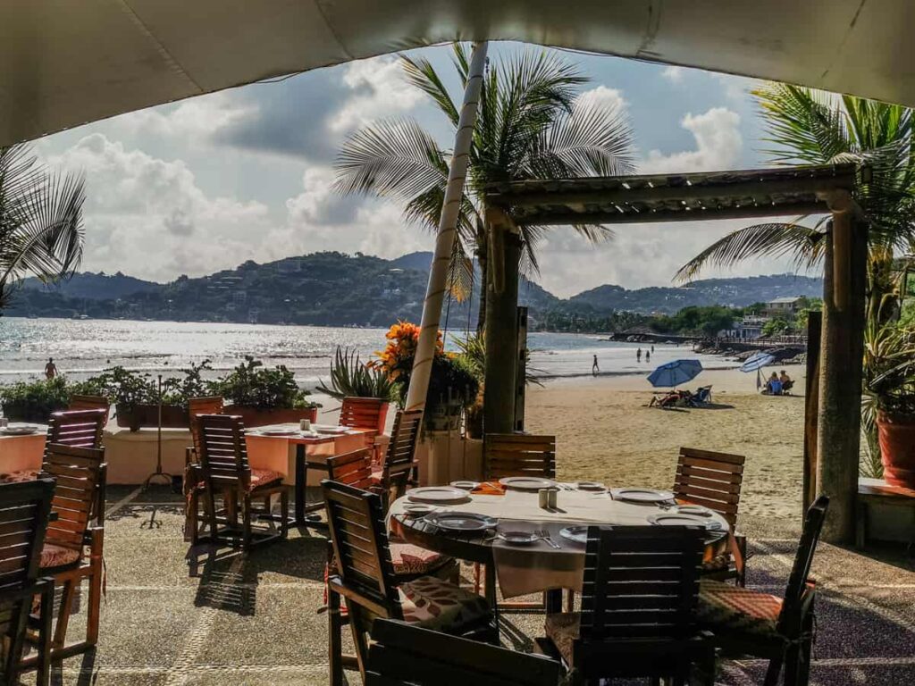 An inviting outdoor seating arrangement at a beachfront restaurant in Zihuatanejo, overlooking the scenic bay with tables set for a high end dining experience at one of the best restaurants in Zihuatanejo.