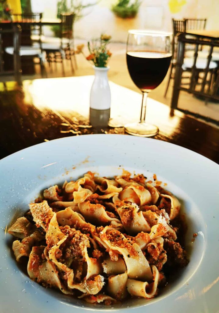 A plate of pappardelle pasta with Bolognese sauce, garnished with grated cheese, presented on a table at the best Italian restaurant in Ixtapa. The setting is elegant with a glass of red wine in the background, offering a refined dining experience.