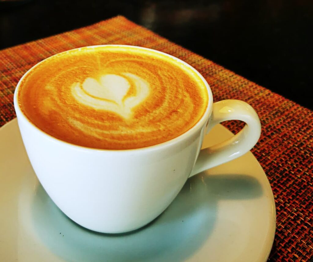 A cappuccino in a white mug with a heart shaped decoration sits on a placemat at a Zihuatanejo cafe.