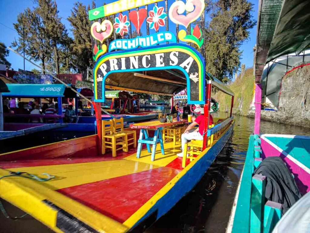 Colorful red, yellow and blue boat in Xochimilco, Mexico City with a sign board "Princesa", a long table and chairs for tourists.
